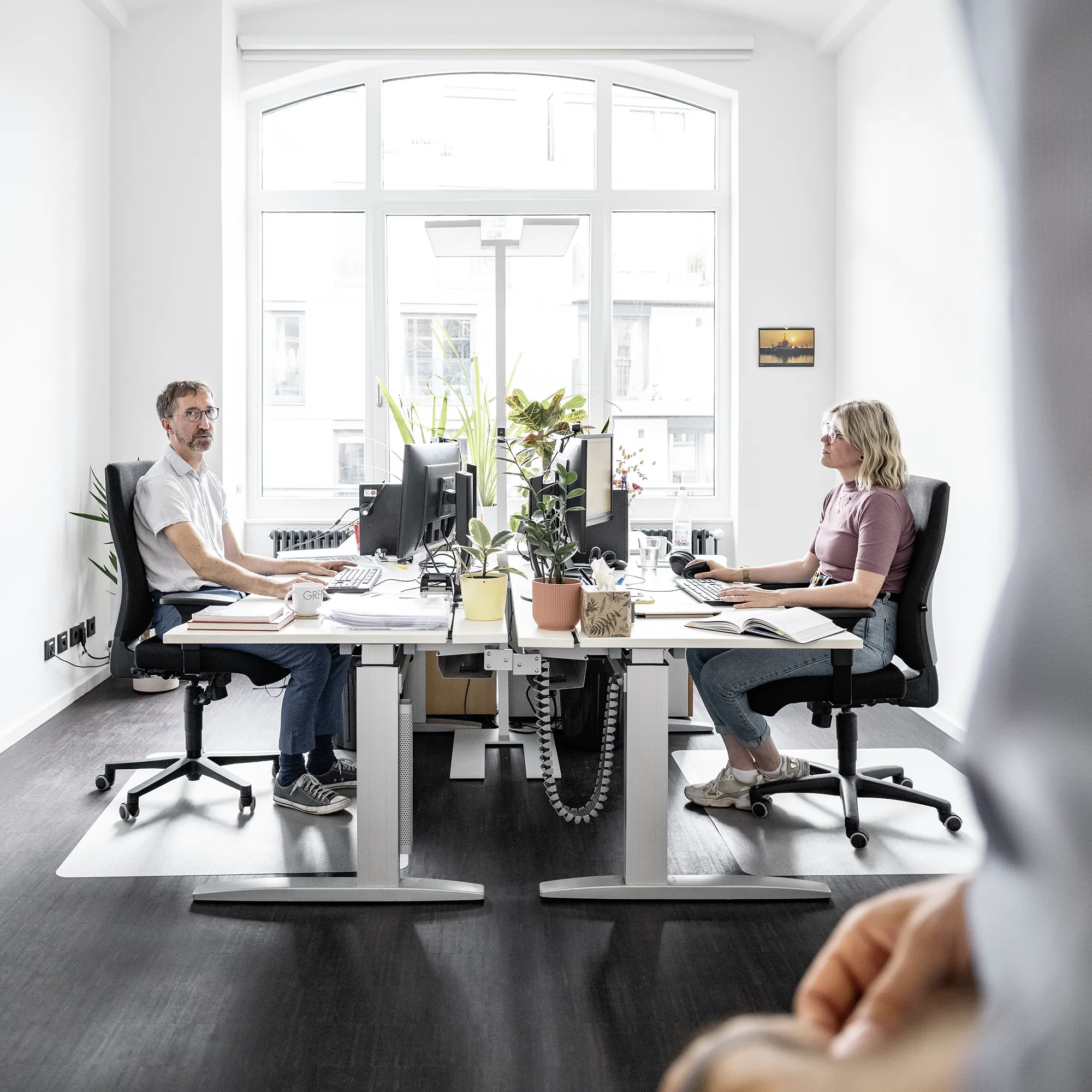 Das Bild zeigt zwei Mitarbeiter im gemeinsamen Büro am arbeiten.